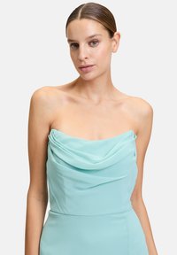 Sukienka bez ramiączek w jasnym odcieniu turkusowym z szyfonu, z zasłoniętym dekoltem i dopasowanym krojem. Gładka tekstura, zaprojektowana na formalne okazje.