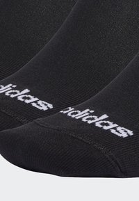 Calcetines deportivos negros con textura acanalada, punta redondeada y el logo de "adidas" en blanco. Diseñados para la comodidad y la durabilidad.