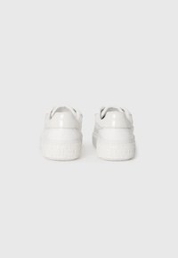 Valged sneakers, millel on siled sünteetiline pealne, ümmargune nina ja tekstuuriga kummine talla, kus on lilleline muster. Seljaosas on väljapaistev brändinimi.