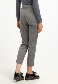 Grå rutiga byxor med skräddarsydd passform, avsmalnande ben och sidofickor, ihopparade med svarta lackskor och en långärmad tröja.