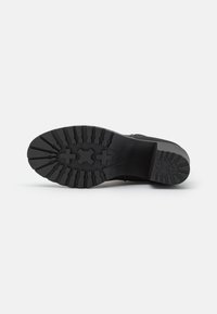 Suela de bota de goma negra con profundos surcos y patrones cruzados; bordes lisos; talón reforzado para tracción y durabilidad.