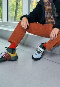 Skor med en blandning av grå, grön och röd färg, med en framträdande Nike-logotyp. Designen inkluderar snörningsdetaljer och texturerade tygdetaljer.