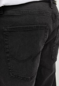 Jeans in denim nero con una finitura texturizzata, dotati di tasche posteriori standard e dettagli di cucitura visibili lungo le cuciture.