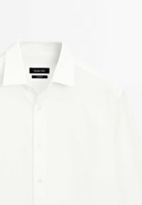 Chemise blanche à boutons avec col classique, partiellement boutonnée, montrant l'étiquette de la marque Massimo Dutti à l'intérieur du col.