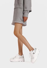 Sneaker platform bianchi con un'accoppiatura argentata a motivo, design con lacci e suola testurizzata. Indossati con un outfit grigio.