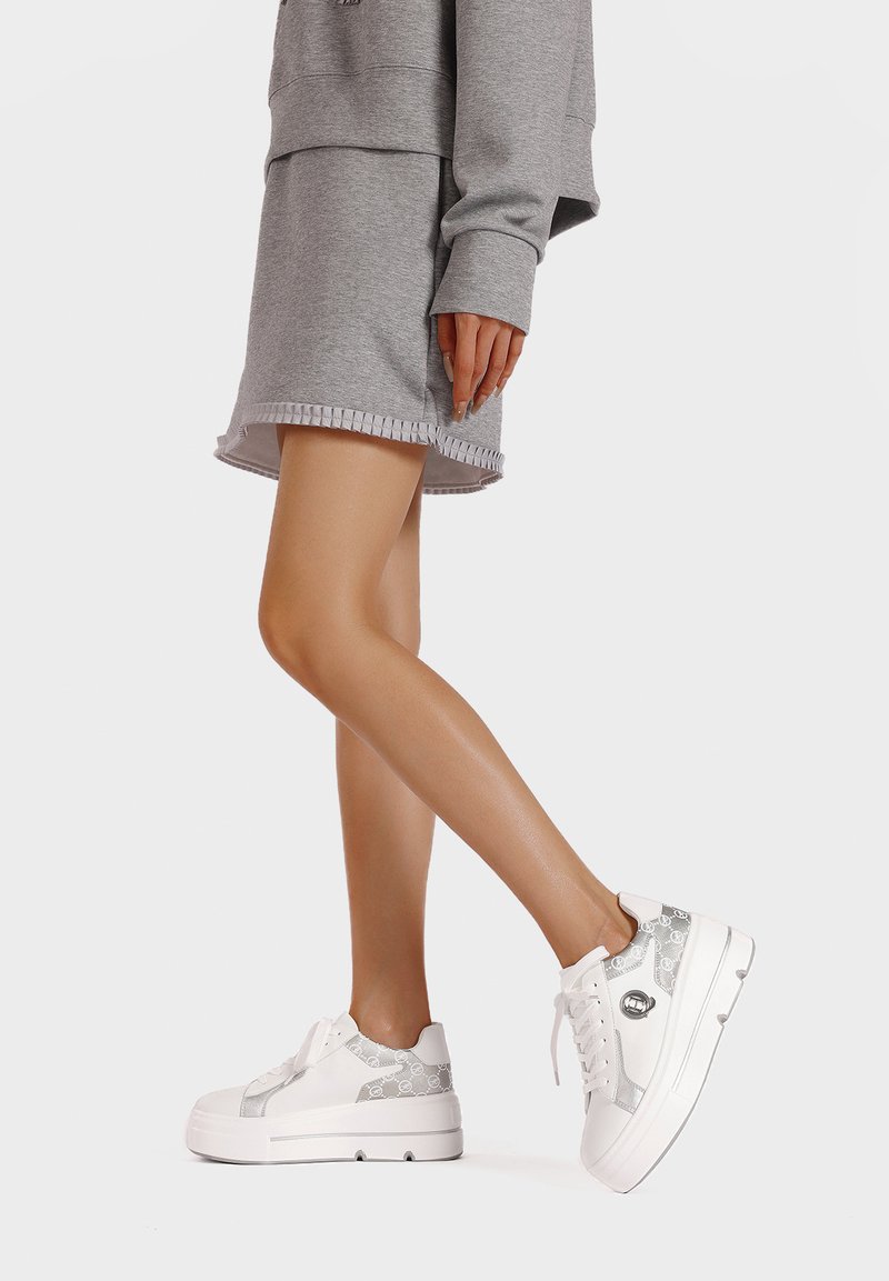 Sneaker platform bianchi con un'accoppiatura argentata a motivo, design con lacci e suola testurizzata. Indossati con un outfit grigio.