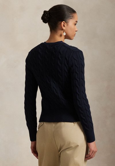 Marineblå kabelstrikket genser med ribbet nederkant og mansjetter, med en tettsittende silhuett. Stoffet har et teksturert, koselig utseende.