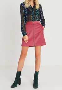 Transparante zwarte blouse met blauw en groen dierenprint; roze corduroy rok met voorrits; enkellaarsjes van donkergroen suede.