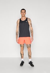 Must must ja väike logo, millele on lisatud oranžid lühikesed püksid. Komplektil on sile tekstuur ja sportlik disain, mida täiustavad mustad spordijalatsid.