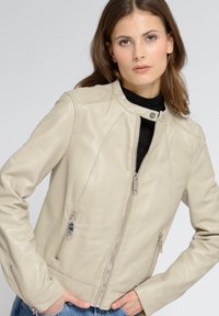 Beige Leder-Motorradjacke mit hohem Kragen, durchgehendem Reißverschluss und seitlichen Taschen. Verfügt über taillierte Nähte und silberne Metallakzente.