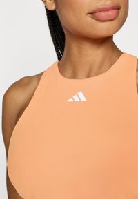 Orange sports top made from smooth fabric featuring a rounded neckline and a white logo accent on the chest area.