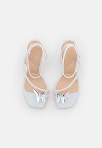 Sandali bianchi con cinturini e parte superiore glitterata e iridescente, con un'accattivante decorazione a forma di farfalla sulla punta. Soletta morbida color beige e design a punta quadrata.