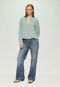 Haut à manches longues vert clair avec un col en V, associé à un jean en denim bleu à jambes larges. Design simple, texture lisse et coupe décontractée.