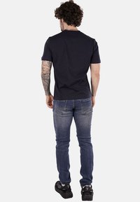 T-shirt a manica corta blu navy abbinato a jeans skinny blu chiaro, con dettagli di leggero sbiadimento, e calzature grigie con accenti neri.