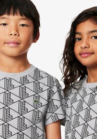 T-shirt grigie con un motivo geometrico nero, caratterizzate da un piccolo logo verde. Design a maniche corte e scollo tondo.