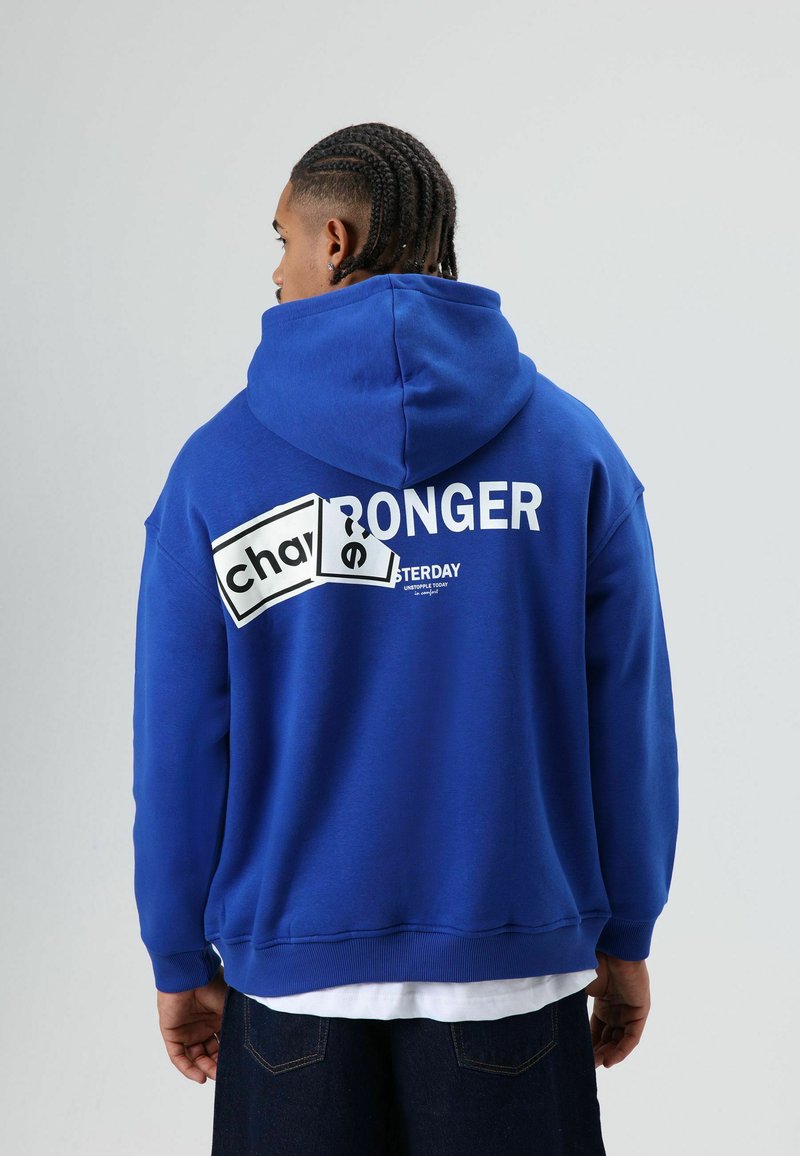 Blauwe hoodie gemaakt van zachte stof. Heeft witte tekst op de achterkant met een rechthoekig patroon. Mouwen en zoom zijn geribd.