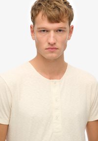 Creme kortærmet henley T-shirt med rund halsudskæring, subtil tekstur og femknaps placketdetalje på brystet.