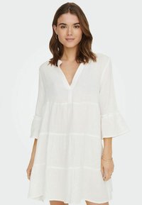 Weißes knielanges Kleid aus leichtem Stoff, mit V-Ausschnitt, dreiviertellangen Glockenärmeln und gestaffeltem Design mit subtiler Textur.