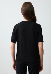 Zwart gebreid T-shirt met korte mouwen en een ronde halslijn. Heeft een gladde textuur en een aansluitende pasvorm bij de taille.