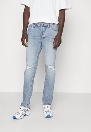 Light blue denim jeans with a regular fit, featuring ripped knee details and a classic five-pocket design. Paired with white and blue sneakers.