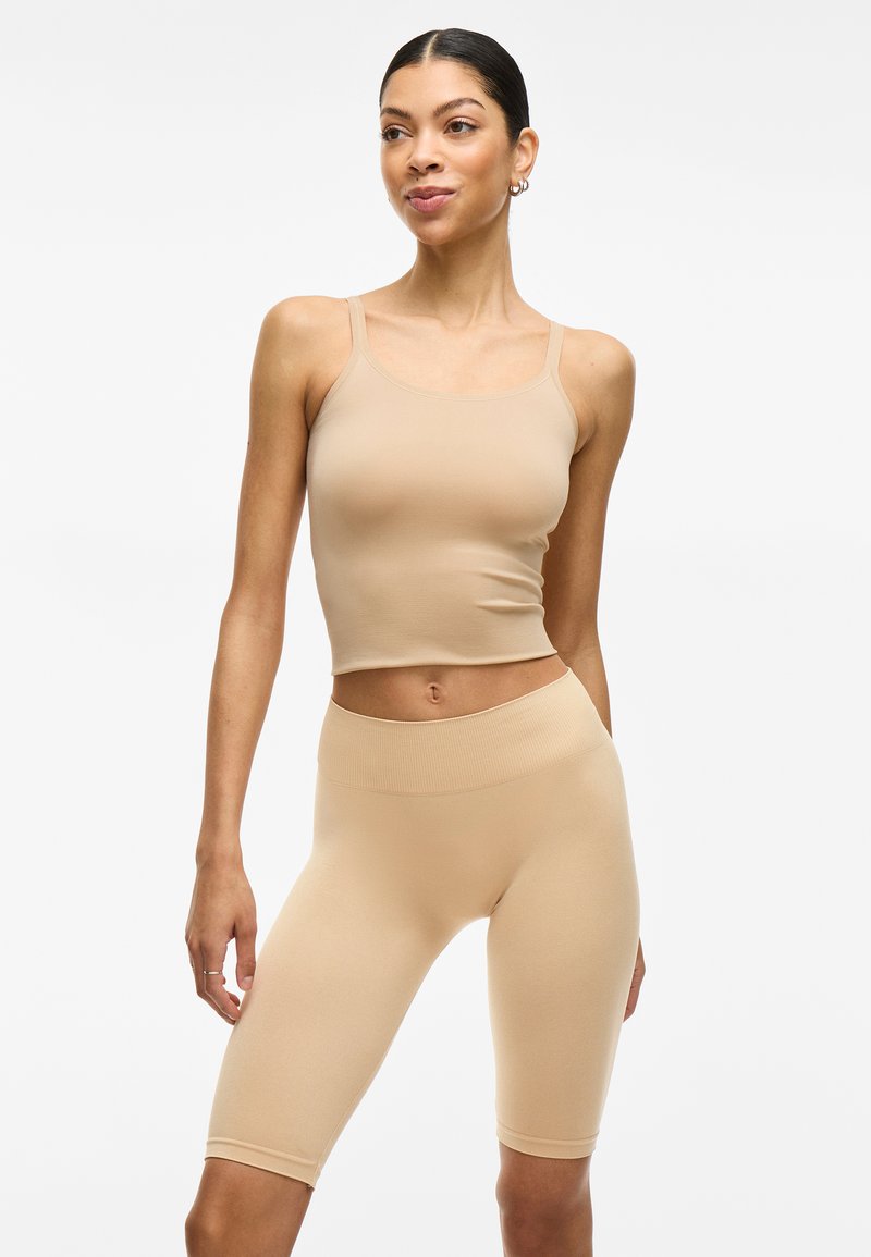 Top corto de tirantes ajustado color beige y pantalones cortos de ciclista de cintura alta, hechos de una suave tela elástica, con tirantes delgados y una cinturilla acanalada.