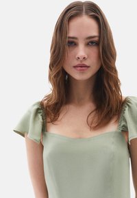 Sukienka w kolorze szałwii z kwadratowym dekoltem oraz bufiastymi rękawami, charakteryzująca się gładką teksturą materiału i luźnym krojem, bez wzorów ani ozdób.