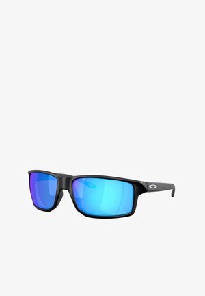 Gafas de sol deportivas negras con montura grande y angular. Lentes espejados azules con acentos morados. Logo distintivo en el brazo lateral.