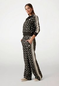 Ensemble de survêtement deux pièces noir comprenant une veste à capuche à motif avec des bandes crème, assortie à un pantalon à jambes larges. Matière douce avec poches.