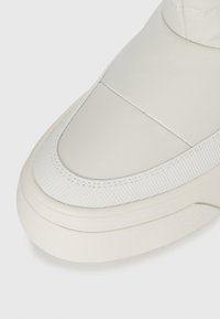 Nærbilde av en lys beige sneakerstøvel med strukturert kant og glatt tekstiloverdel på hvit bakgrunn.