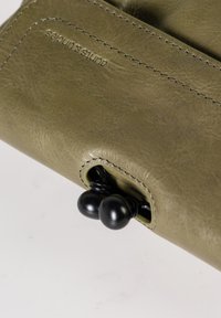 Portafoglio in pelle verde con cuciture visibili, dotato di meccanismo di chiusura arrotondato e accenti in metallo nero. Texture liscia con finitura opaca.