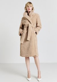 Accappatoio beige e soffice realizzato in materiale morbido e testurizzato. Presenta un colletto e una cintura, con due tasche laterali, design fino al ginocchio e maniche lunghe.