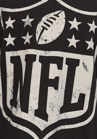 Maglietta nera con un grande logo NFL invecchiato, accompagnato da un pallone da football e cinque stelle bianche sopra. Il design grafico è stampato in bianco a contrasto.