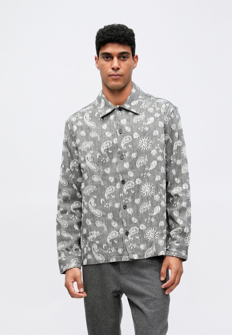 Halli halliga hall värvi särk, millel on valged paisley mustrid, krae ja pikad varrukad. Kombineeritud hallide pükstega. Kangas näeb välja tekstuurne.