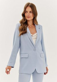 Světle modrý blazer s klopovým límcem, zapínáním na jeden knoflík a dvěma předními kapsami. Hladká textura s přiléhavým střihem.