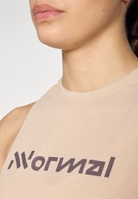 Beige ermeløs sportstopp med teksturert stoff og rutemønster, samt en mørk logo på brystområdet.