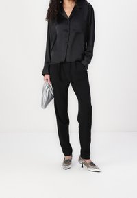 Svart satin skjorta med knappar kombinerad med svarta byxor, silverhandväska och metalliska klackar. Släta texturer med en avslappnad passform.