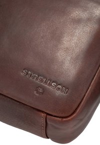 Borsa in pelle marrone con superficie testurizzata, bordi arrotondati e logo "Strellson" in rilievo sul fronte. Presenta accenti di cucitura visibili.