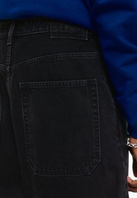 Sorte denim jeans har en stor baglomme og en struktureret talje. Materialet virker holdbart, med subtile syninger.