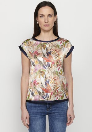 Haut en satin avec un motif floral multicolore, manches courtes et accents navy au col et à l'ourlet. Texture lisse. Porté avec un jean en denim.