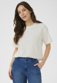 Vit kortärmad T-shirt i lätt material, med rund halsringning och avslappnad passform, tillsammans med blå högmidjade jeans.
