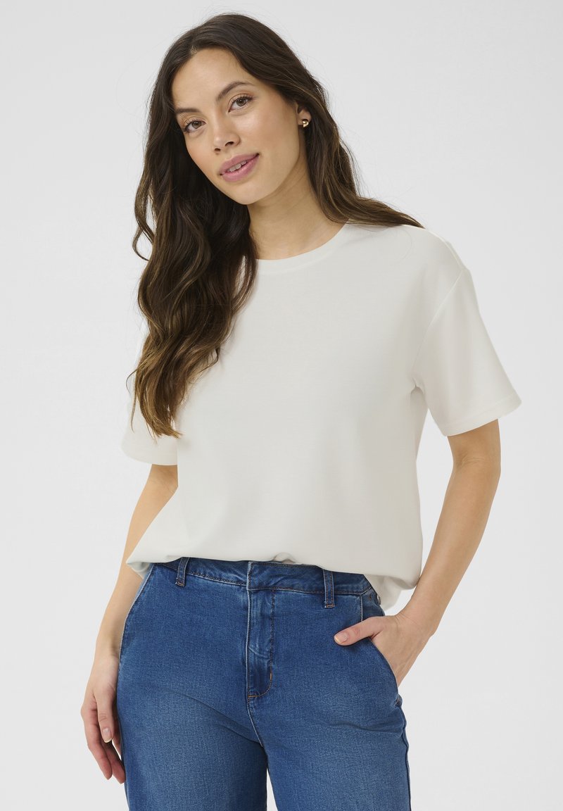 Vit kortärmad T-shirt i lätt material, med rund halsringning och avslappnad passform, tillsammans med blå högmidjade jeans.