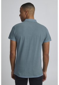 Kortærmet polo-shirt i dæmpet blå, har en krave, blød tekstur og en lige kant med en let sidesplit nederst.
