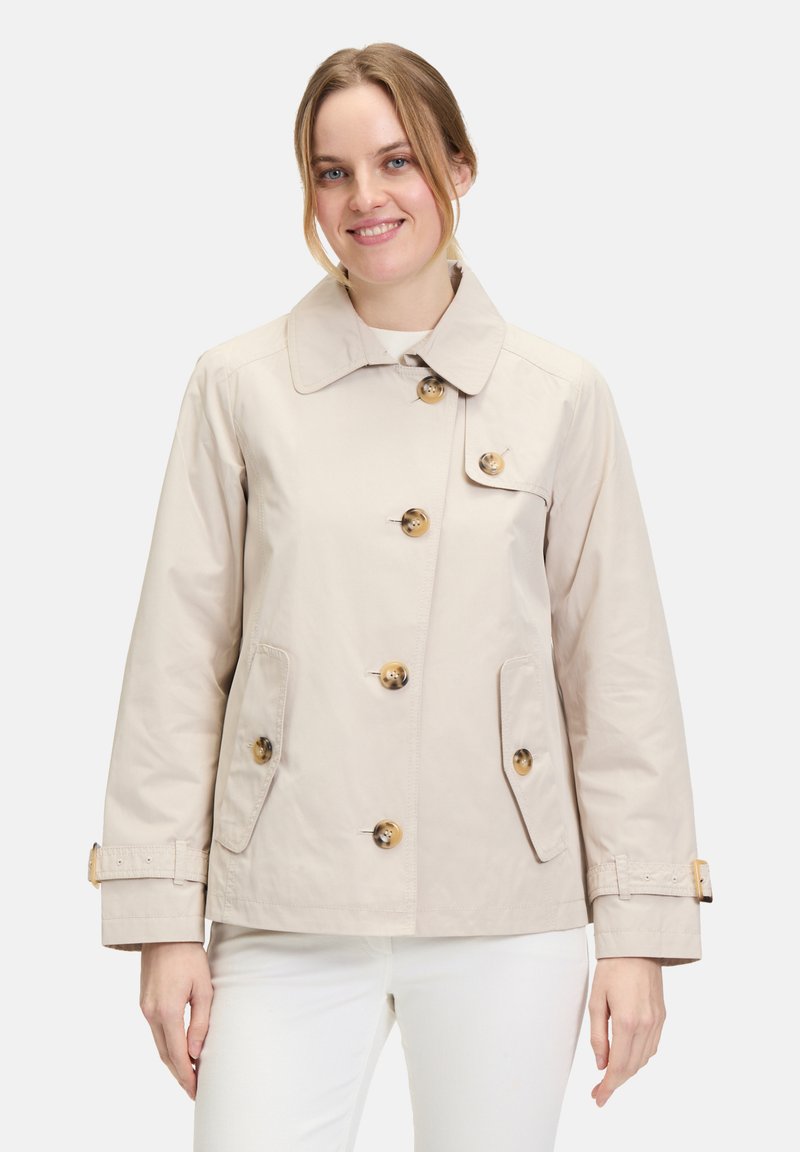 Beige Trenchcoat mit klassischem Schnitt, ausgestattet mit großen Knöpfen, zwei Fronttaschen und einem breiten Kragen. Hergestellt aus einem glatten, leichten Stoff.