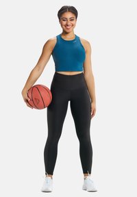 Türkiisi crop top, mis on kombineeritud kõrge vöökohaga mustade retuusidega, hoiab korvpalli; valged spordijalatsid täiendavad sportlikku välimust.