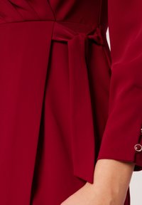 Czerwona sukienka z paskiem o drapowanej konstrukcji, z gładką fakturą i eleganckimi guzikami na rękawach.