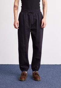 Black cotton joggers with an elastic waistband and drawstring, featuring cuffed ankles and a small logo detail near the pocket.