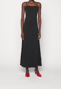 Czarna, bezrękawnikowa maxi sukienka o kwadratowym dekolcie, wykonana z gładkiego materiału. W zestawieniu z błyszczącymi, czerwonymi sandałkami na obcasie.