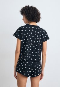 Schwarzes T-Shirt mit kurzen Ärmel und kurze Hosen Set mit einem all-over weißen Cartoon-Druck. Leichter Stoff mit lässigem Schnitt und Saum auf Taillenhöhe.