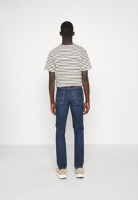 Striped short-sleeve shirt in shades of beige and green, paired with dark blue straight-leg jeans and light sneakers, viewed from the back.