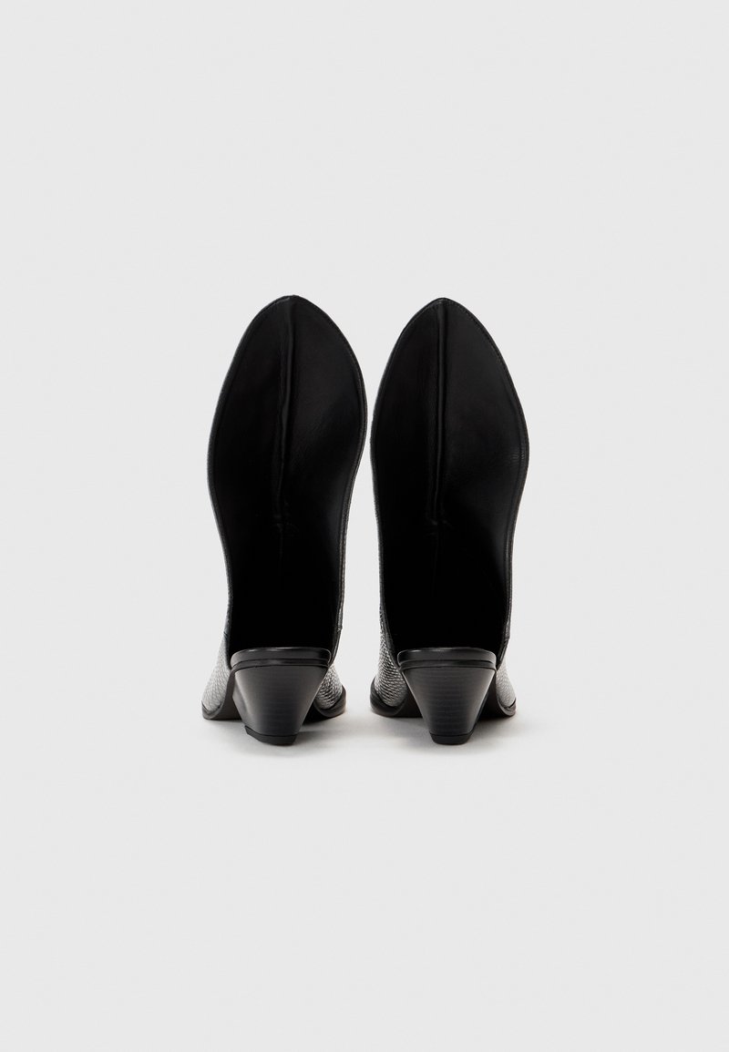 Chaussures à talon compensé en cuir noir avec un design à bout pointu et un motif texturé. Les talons sont coniques et présentent une finition lisse en noir.